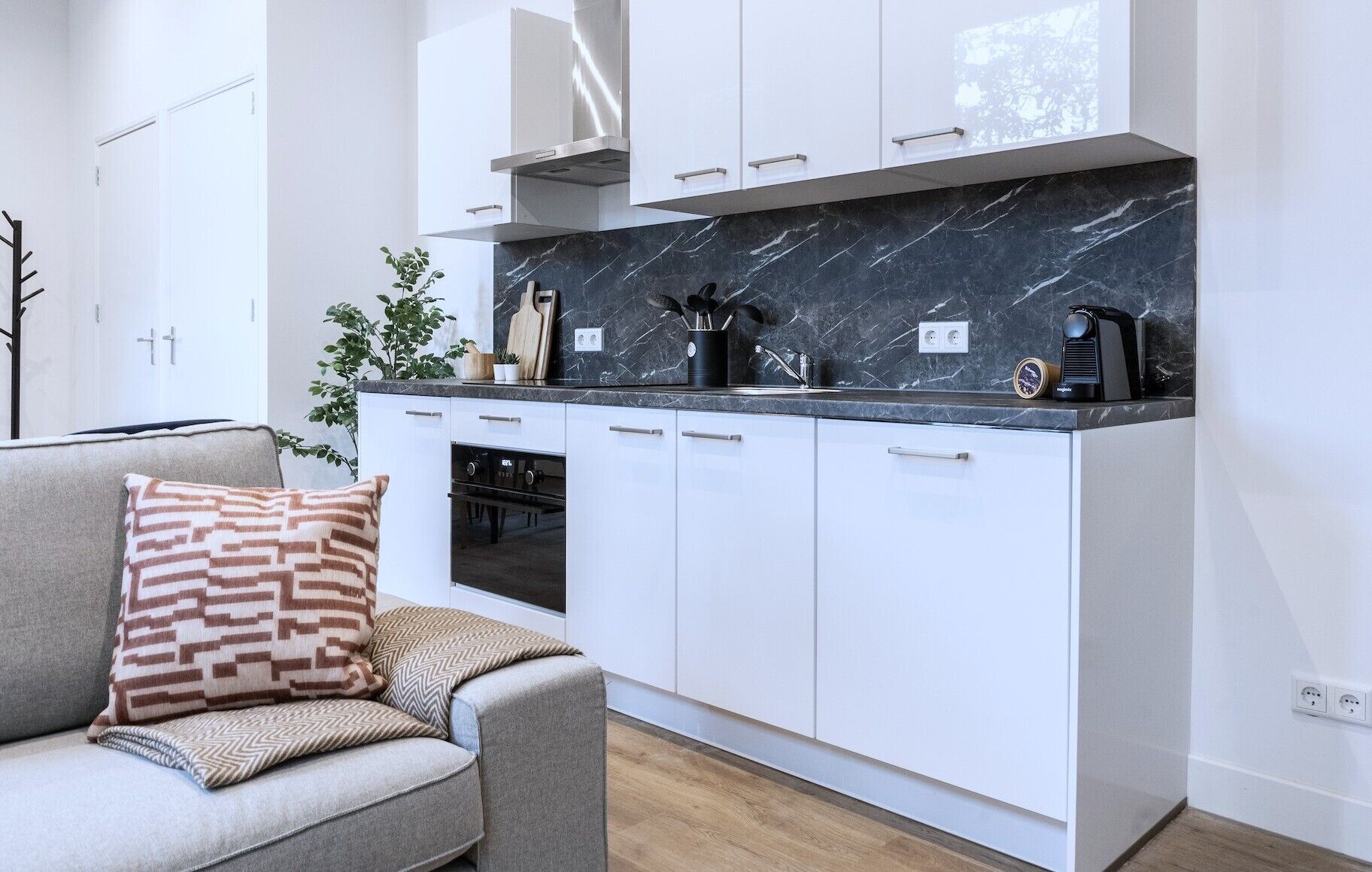 Una cocina moderna con armarios blancos, encimera de mármol y horno empotrado.
