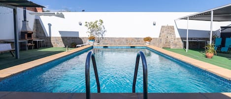 Piscina com muro de pedra e céu azul límpido.