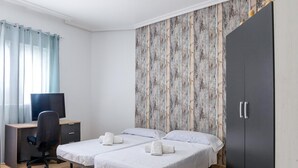 Une chambre avec deux lits, un bureau, une chaise, une armoire et un téléviseur.