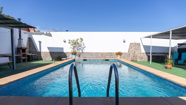 Une piscine avec un mur en pierre et un bâtiment blanc en arrière-plan.