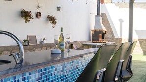 Un espace bar extérieur avec une piscine carrelée, des tabourets de bar, une bouteille de vin et un barbecue.
