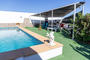 Une piscine dotée d’un patio couvert, d’un espace salon extérieur et d’un mur en pierre.
