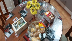 Een ronde tafel met een glazen blad, versierd met een zonnebloem als middelpunt, een schaal met snacks en een doos koekjes.