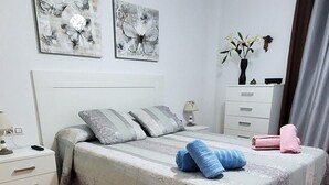 Een slaapkamer met een bed, kussens, een nachtkastje, een dressoir en kunst aan de muur.