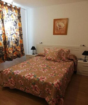 Ein Schlafzimmer mit floralem Bettbezug, einem Einzelbett mit passenden Kissen, zwei Nachttischen mit Lampen sowie einem Wandbild.