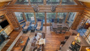 Un intérieur spacieux de chalet en bois, avec un plafond haut, des poutres apparentes, une cheminée et un coin repas.
