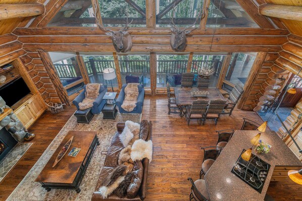 A spacious log cabin interior with a high ceiling, wooden beams, a fireplace, and a dining area. - High Noon Lodge-Curate Telluride, Views, Hot tub, 5 bed, Fireplace, Private (Mountain Village)