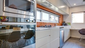 A modern kitchen with stainless steel appliances, white cabinetry, and a dining area with black chairs. - Cosy 1-bedroom Apartment Close to the City (Sydney)