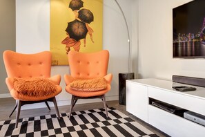 Un salon moderne avec deux fauteuils orange, un meuble de rangement blanc et un grand téléviseur à écran plat fixé au mur.