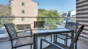 A balcony with a glass table and chairs, a view of a brick building, and parked cars. - Cosy 1-bedroom Apartment Close to the City (Sydney)