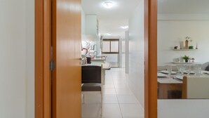A hallway leading to a dining area with a table set for two, a chair, and a small shelf with decorative items. - 5 minutes from Macumba Beach | ZV101 (Rio de Janeiro)