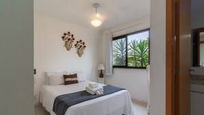 A hotel room with a bed, a window with a view of greenery, a wall-mounted light fixture, and a small table with a lamp. - 5 minutes from Macumba Beach | ZV101 (Rio de Janeiro)