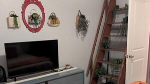 Een slaapkamer met een bed, een dressoir, een televisie en wandplanters.