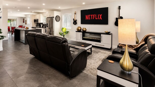 Ein modernes Wohnzimmer mit einem schwarzen Ledersofa, einem Couchtisch und einem an der Wand montierten Fernseher, der 'NETFLIX' anzeigt.