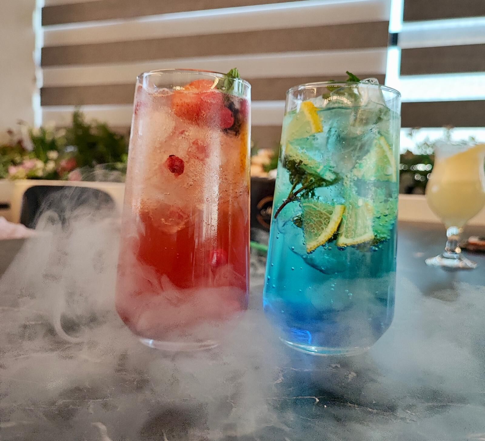 Two glasses of iced drinks on a table with steam rising from the surface.