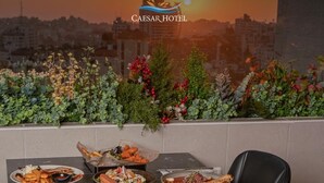 A dining table with various dishes, a cityscape view, and a Caesar Hotel logo. - Caesar Hotel (Ramallah)