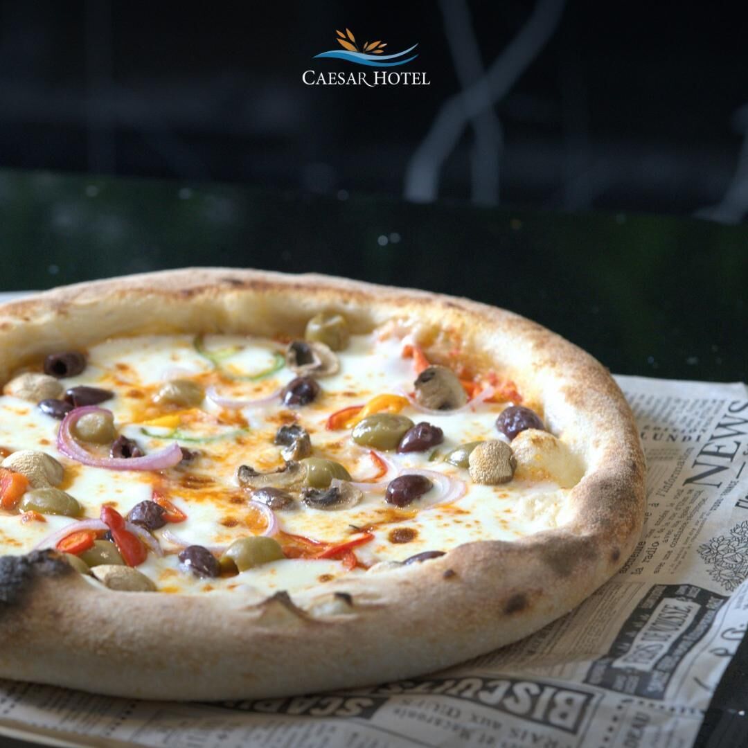 Pizza con distintos ingredientes sobre una mesa, con un periódico debajo.