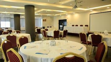 A conference room with round tables, red upholstered chairs, and a projector screen.