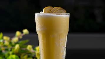 A tall glass with a yellow beverage, ice cubes, and a lemon slice on a green surface.