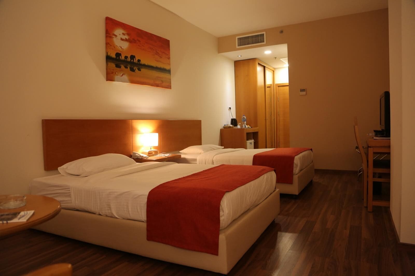 Habitación de hotel con dos camas, un escritorio, una silla, un televisor y un cuadro en la pared.