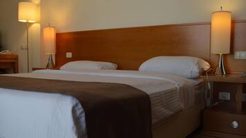 A hotel room with a large bed, two bedside lamps, a wooden headboard, and a nightstand with a phone and a lamp.