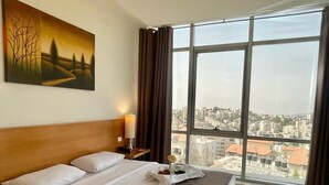 A hotel room with a large bed, a nightstand, a lamp, and a painting on the wall. - Caesar Hotel (Ramallah)