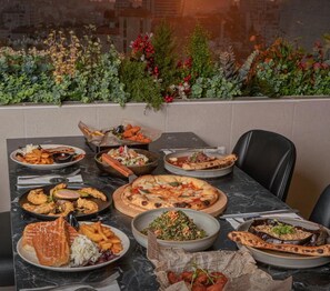 A dining table with various dishes, a cityscape view, and a Caesar Hotel logo. - Caesar Hotel (Ramallah)