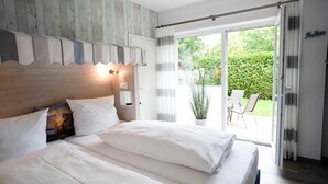 Ein Schlafzimmer mit Holz-Kopfteil, einem großen Bett mit weißer Bettwäsche, einem Nachttisch mit Lampe und einer Schiebetür zu einer Terrasse mit Stühlen und einem Tisch.