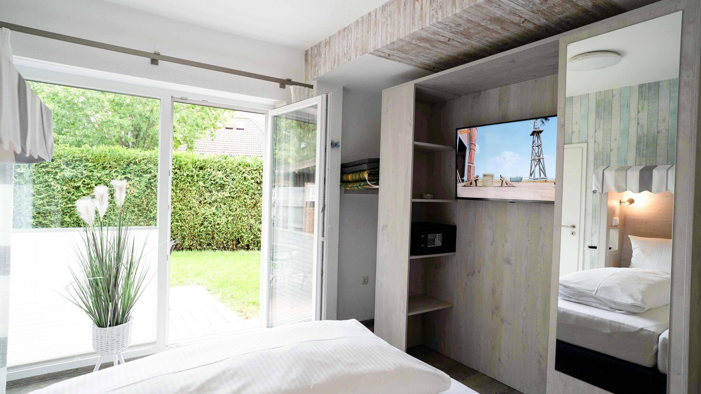 A bedroom with a bed, a TV mounted on the wall, and a sliding door leading to a garden.