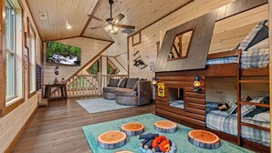 L’intérieur d’une cabane comprend un lit en mezzanine, un canapé, un téléviseur et un plancher en bois.
