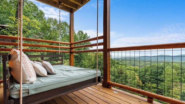 Une terrasse en bois avec un hamac suspendu, entourée d’une balustrade en bois, offrant une vue sur un paysage boisé.