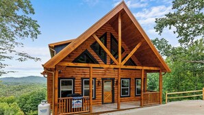 Une cabane en rondins avec un toit triangulaire, de grandes fenêtres et une véranda.