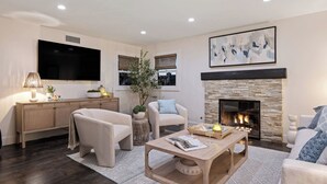 Ein modernes Wohnzimmer mit Kamin, bequemen Sitzmöglichkeiten, einem Flachbildfernseher und einem großen abstrakten Gemälde.