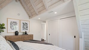 Ein Schlafzimmer mit einem großen Bett, einer Holzkommode, zwei gerahmten Kunstwerken und einem weißen Kleiderschrank.