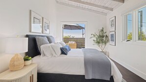 Ein Schlafzimmer mit Bett, Nachttisch, Lampe, Pflanze und gerahmten Bildern an der Wand.