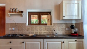 A kitchen with a stove, sink, wooden cabinets, a window, and a shelf with jars. - Holiday Home 'Domo Clelia' with Private Terrace, Garden & Air Conditioning (Nulvi)