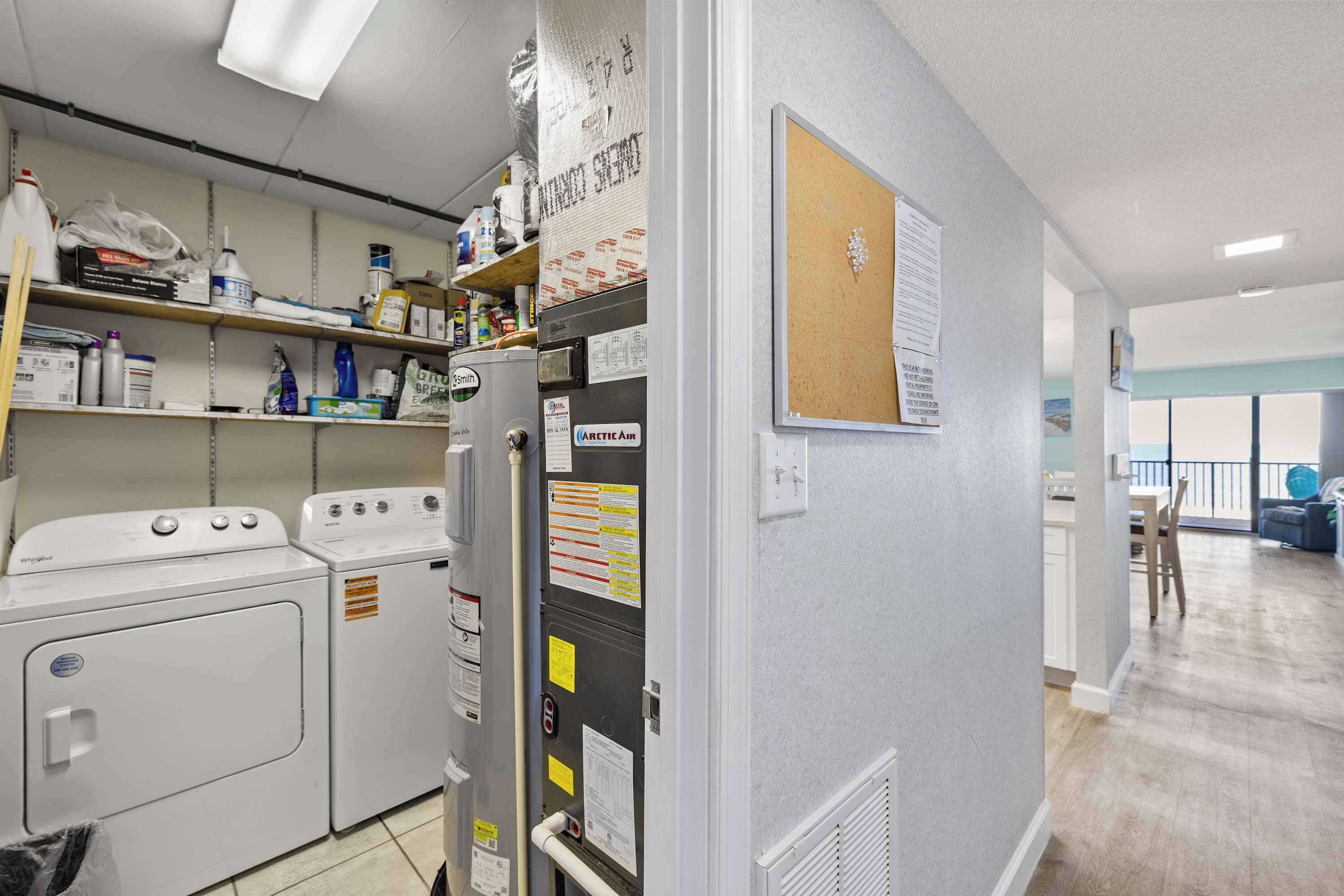 A laundry room with two washing machines, a dryer, and a utility panel with various labels and instructions.
