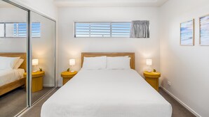 Ein Hotelzimmer mit einem großen Bett, zwei Nachttischen mit Lampen, einem Fenster mit Jalousien und einem Spiegel an einer Wand.