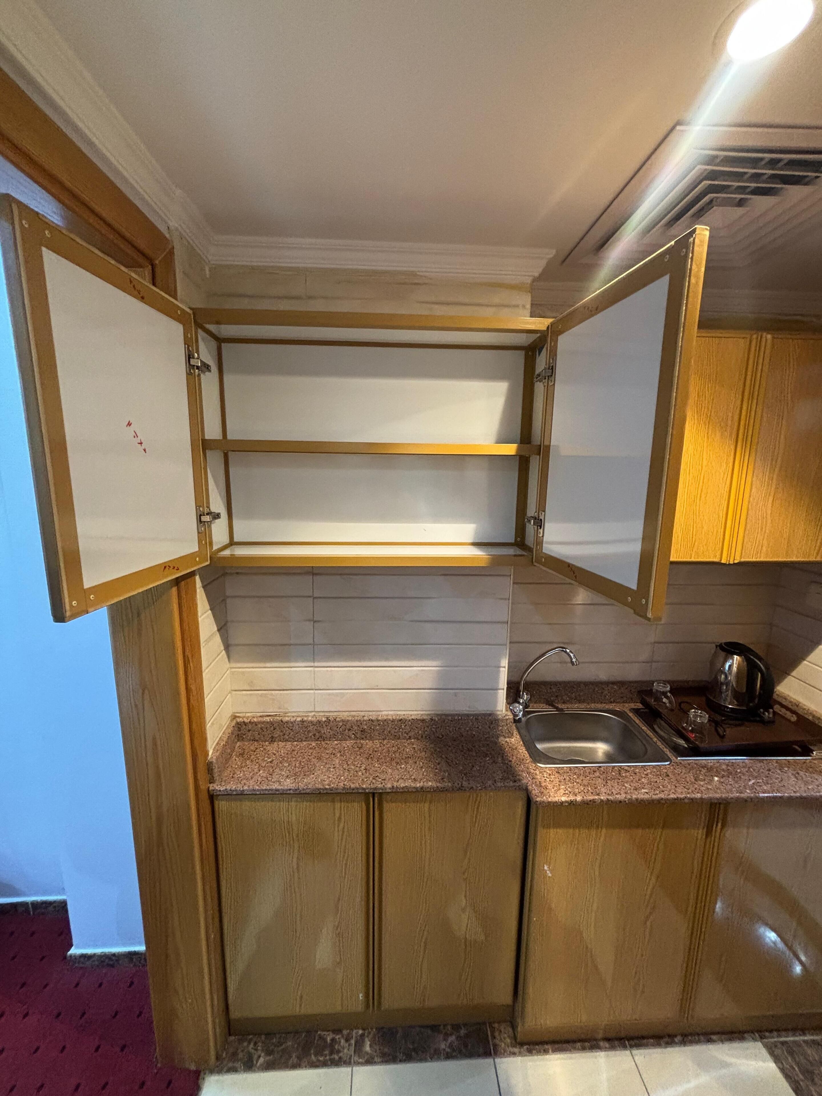 Eine kleine Küche mit Holzausstattung, einer Arbeitsplatte aus Granit, einer Edelstahl-Spüle und einem Wasserkocher.