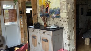 Un intérieur rustique avec un plafond en bois, une horloge noire, un tableau et un coin repas avec une nappe à carreaux.