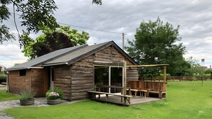 Une cabane en bois dotée d’une terrasse, d’un espace salon couvert et d’une grande fenêtre.