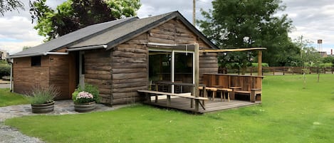 A wooden cabin with a patio, a covered seating area, and a large window.