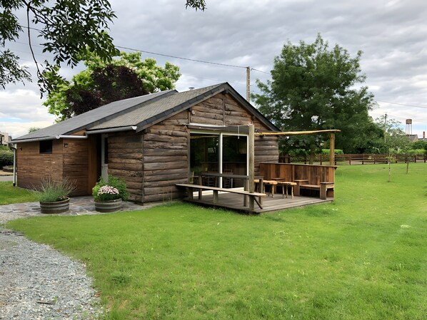 Une cabane en bois dotée d’une terrasse, d’un espace salon couvert et d’une grande fenêtre.