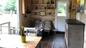 Une cabane aux murs en bois, un coin repas avec une table et des chaises, un espace détente avec un canapé et une petite cuisine équipée d’un réfrigérateur.