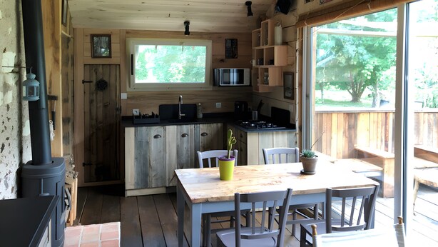 Un chalet rustique en bois, doté d’une cuisine, d’un coin repas et de grandes fenêtres.