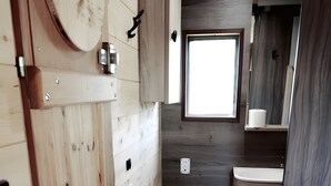 Ein kleines Badezimmer aus Holz mit Toilette, Waschbecken und Fenster.