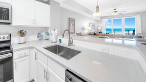 A modern kitchen with white cabinetry, a stainless steel sink, and a built-in oven. - ☀️Panoramic Gulf and Pool Views-Steps to Beach-Calypso 3-1006☀️ (Panama City Beach)