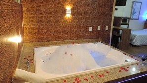 A bathroom with a large bathtub, a wooden wall, and a small seating area. - Cabanas Costaneira  (Cambará do Sul)