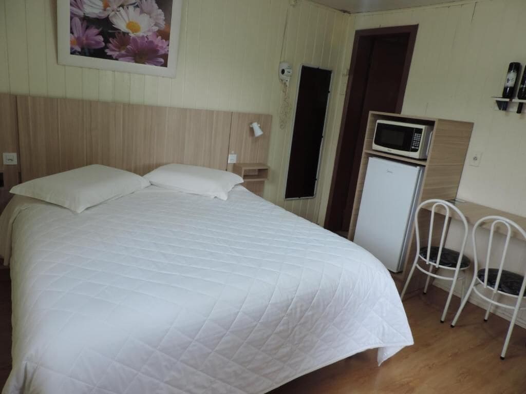 A hotel room with a large bed, a small refrigerator, a microwave, and a chair.
