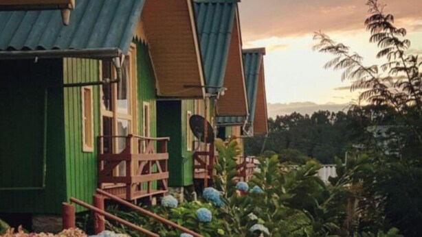 A row of colorful, wooden cabins with a balcony, surrounded by lush greenery and a scenic view. - Cabanas Costaneira  (Cambará do Sul)